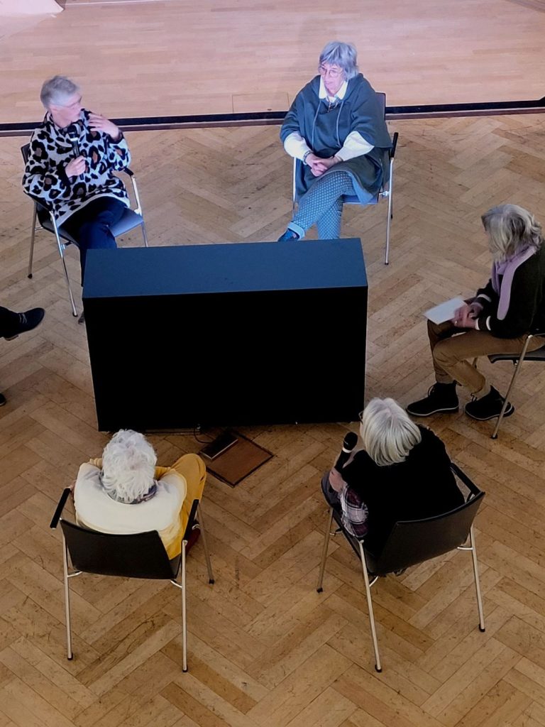 Fünf Frauen sitzen in einem Stuhlkreis im Saal.