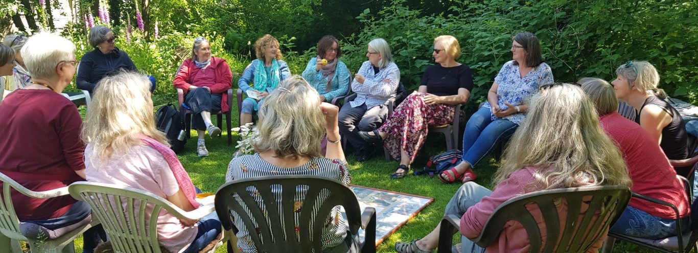 Eine Gruppe von Frauen sitzt im Stuhlkreis im Garten.